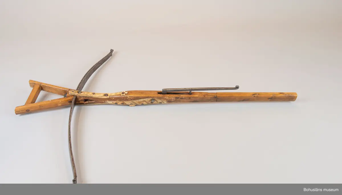 Mått forts. Stocken 5 cm tjock, 107,5 cm lång, stålbågen 92,5 cm lång; fotbygeln 12 x 14 cm.

Kraftig handsmidd stålbåge fastgjord mot trästocken med handsmidd nit med kvadratiskt huvud. Iläggningar med dekorskurna plattor av horn, placerade utmed stockens alla sidor på stockens nedre halva. Hornet är  dekorerat med rika yttäckande mörkfärgade ristningar av samisk typ och är fästade med handsmidd spik och en modern spårskruv. En hornplatta saknas. Armborstnöt med anläggningsyta och axel av järn 
Kantig fotbygel av trä, senare komplettering. Kort pilränna, lång smidd avtryckare med  rullad ände, fästad i stocken med senare mutter och skruv.
Bågstängen av rep, senare komplettering.
Bågens  infästning är otypisk och ej lika kraftig som dessa brukar vara och är därför troligen ett senare tillägg.

Ur handskrivna katalogen 1957-1958:
Armborst, Lappbåge
L. 107,5, bågen: 89,5 cm; järnbåge, i övr. trä och ben, d. senare m. inristad dekor; sträng av flätat snöre. Rostig.

Lappkatalog: 7

Se Länkad fil/Referenser samt Bilagepärmen med kompletterande upplysningar  för UM002484 och UM001154 i brev från Statens Försvarshistoriska Museer, Erik Walberg, konservator Metall -och vapensektionen, december 2002 samt  UM002249 med artikel ur Bohusläningen 19/6 1931; Värdefullt nyförvärv till Uddevalla museum. 
Donation av häradshövding A. M. von Proschwitz.