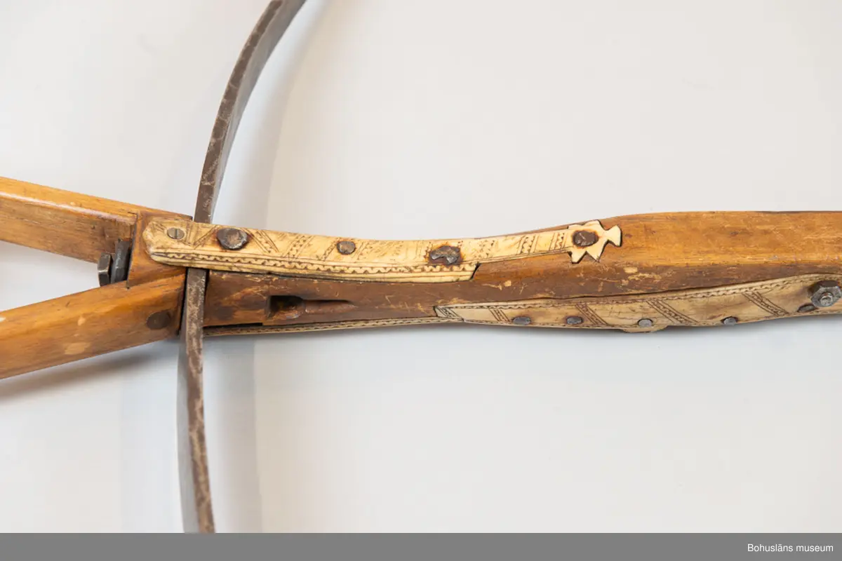 Mått forts. Stocken 5 cm tjock, 107,5 cm lång, stålbågen 92,5 cm lång; fotbygeln 12 x 14 cm.

Kraftig handsmidd stålbåge fastgjord mot trästocken med handsmidd nit med kvadratiskt huvud. Iläggningar med dekorskurna plattor av horn, placerade utmed stockens alla sidor på stockens nedre halva. Hornet är  dekorerat med rika yttäckande mörkfärgade ristningar av samisk typ och är fästade med handsmidd spik och en modern spårskruv. En hornplatta saknas. Armborstnöt med anläggningsyta och axel av järn 
Kantig fotbygel av trä, senare komplettering. Kort pilränna, lång smidd avtryckare med  rullad ände, fästad i stocken med senare mutter och skruv.
Bågstängen av rep, senare komplettering.
Bågens  infästning är otypisk och ej lika kraftig som dessa brukar vara och är därför troligen ett senare tillägg.

Ur handskrivna katalogen 1957-1958:
Armborst, Lappbåge
L. 107,5, bågen: 89,5 cm; järnbåge, i övr. trä och ben, d. senare m. inristad dekor; sträng av flätat snöre. Rostig.

Lappkatalog: 7

Se Länkad fil/Referenser samt Bilagepärmen med kompletterande upplysningar  för UM002484 och UM001154 i brev från Statens Försvarshistoriska Museer, Erik Walberg, konservator Metall -och vapensektionen, december 2002 samt  UM002249 med artikel ur Bohusläningen 19/6 1931; Värdefullt nyförvärv till Uddevalla museum. 
Donation av häradshövding A. M. von Proschwitz.