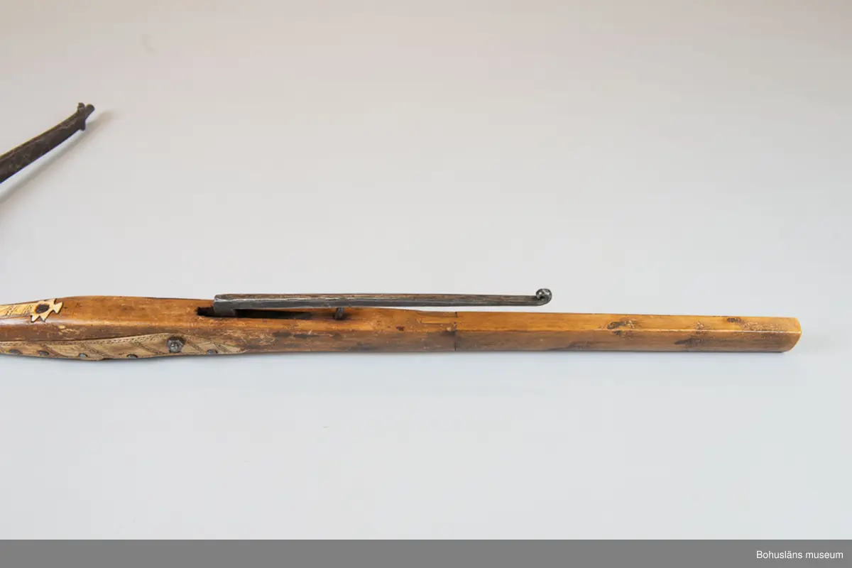 Mått forts. Stocken 5 cm tjock, 107,5 cm lång, stålbågen 92,5 cm lång; fotbygeln 12 x 14 cm.

Kraftig handsmidd stålbåge fastgjord mot trästocken med handsmidd nit med kvadratiskt huvud. Iläggningar med dekorskurna plattor av horn, placerade utmed stockens alla sidor på stockens nedre halva. Hornet är  dekorerat med rika yttäckande mörkfärgade ristningar av samisk typ och är fästade med handsmidd spik och en modern spårskruv. En hornplatta saknas. Armborstnöt med anläggningsyta och axel av järn 
Kantig fotbygel av trä, senare komplettering. Kort pilränna, lång smidd avtryckare med  rullad ände, fästad i stocken med senare mutter och skruv.
Bågstängen av rep, senare komplettering.
Bågens  infästning är otypisk och ej lika kraftig som dessa brukar vara och är därför troligen ett senare tillägg.

Ur handskrivna katalogen 1957-1958:
Armborst, Lappbåge
L. 107,5, bågen: 89,5 cm; järnbåge, i övr. trä och ben, d. senare m. inristad dekor; sträng av flätat snöre. Rostig.

Lappkatalog: 7

Se Länkad fil/Referenser samt Bilagepärmen med kompletterande upplysningar  för UM002484 och UM001154 i brev från Statens Försvarshistoriska Museer, Erik Walberg, konservator Metall -och vapensektionen, december 2002 samt  UM002249 med artikel ur Bohusläningen 19/6 1931; Värdefullt nyförvärv till Uddevalla museum. 
Donation av häradshövding A. M. von Proschwitz.