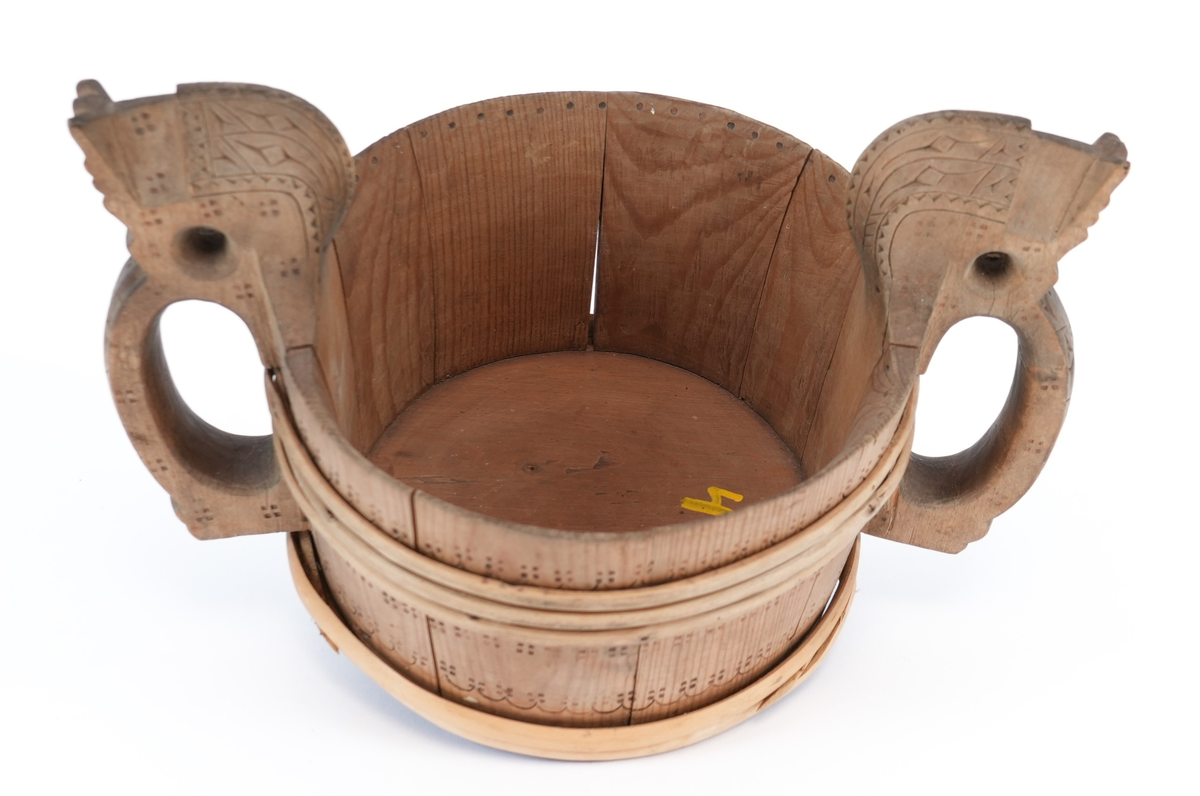 Svidd ornament over heile staupet. På behaldar, rundt vidjeband bord av bylgjelinjer med krossar. Handtaka utskorne i form av stiliserte hestehovud med utskorne sikksakk og pil teikn (?) og svidd krossar. Inni, i øvre kant svidd punkter.