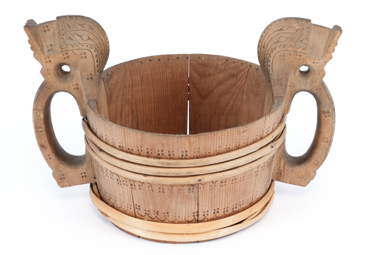 Svidd ornament over heile staupet. På behaldar, rundt vidjeband bord av bylgjelinjer med krossar. Handtaka utskorne i form av stiliserte hestehovud med utskorne sikksakk og pil teikn (?) og svidd krossar. Inni, i øvre kant svidd punkter.