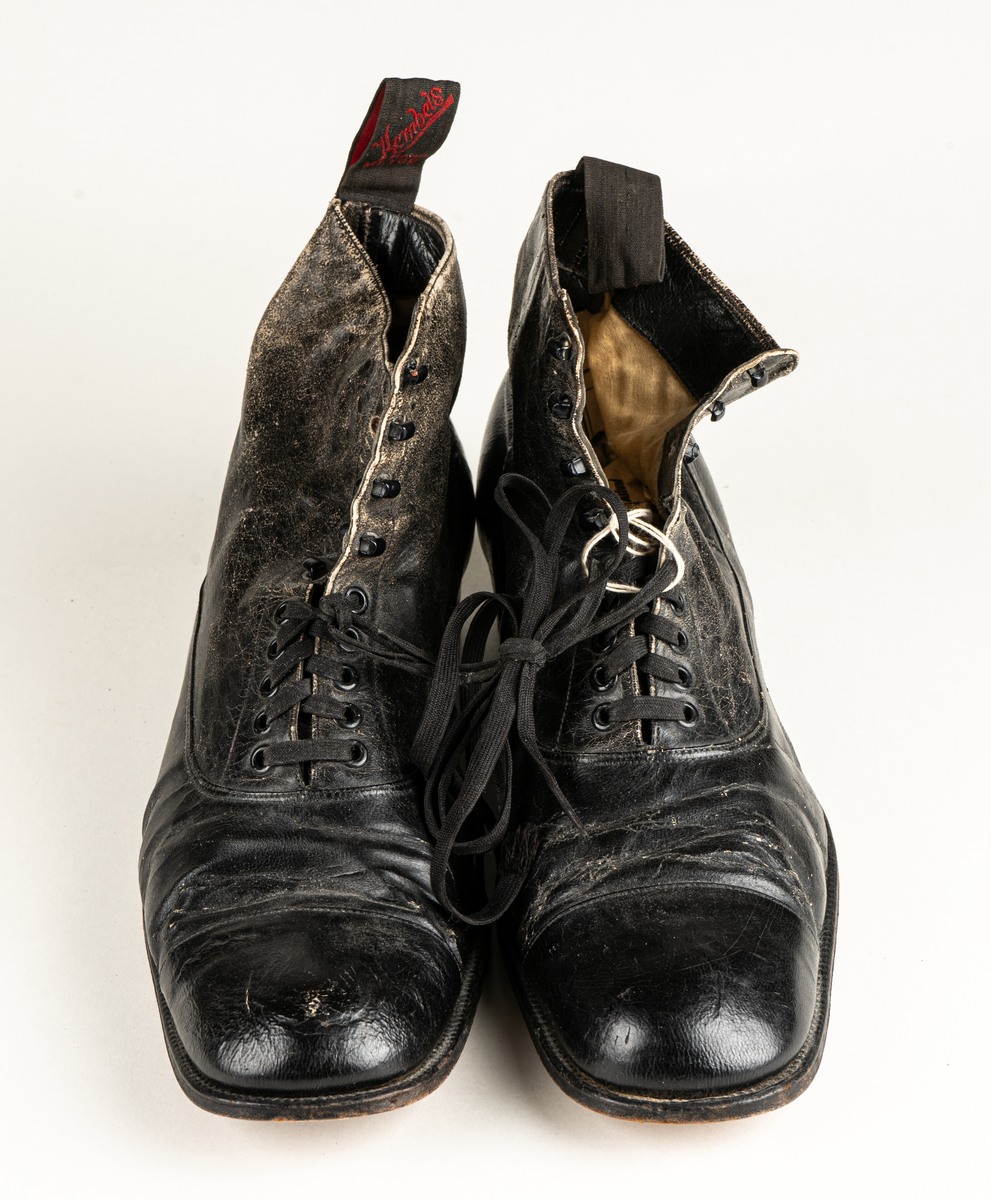 Ett par herrskor i läder som ägts av Karl Fredrik Jernberg, Alfta.  Tidigt 1900-tal. Skorna är svarta med halvhögt skaft. Snörning med både hål och hyskor.