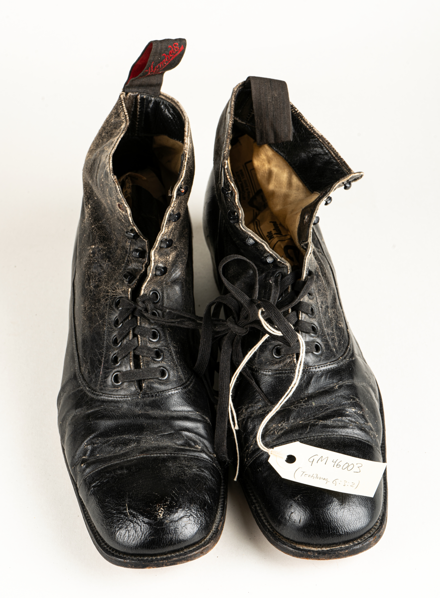 Ett par herrskor i läder som ägts av Karl Fredrik Jernberg, Alfta.  Tidigt 1900-tal. Skorna är svarta med halvhögt skaft. Snörning med både hål och hyskor.