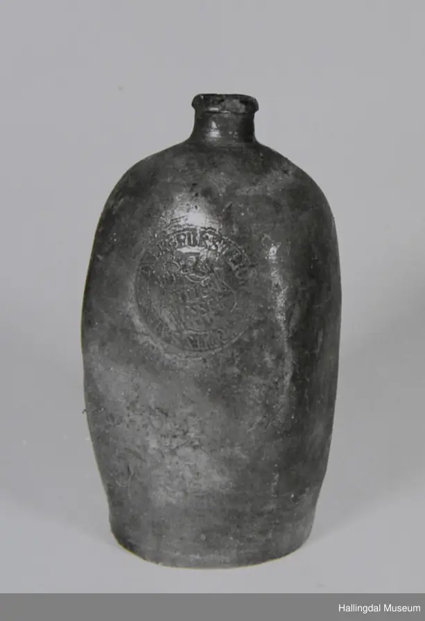 Sirkulær bunn, corpus bunket inn til 4-kantet tverrsnitt. Sylindrisk tut med utvidet munningsrand.