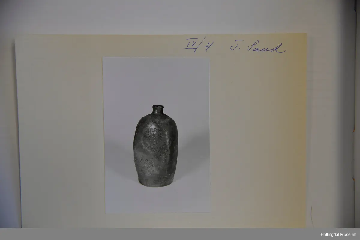 Sirkulær bunn, corpus bunket inn til 4-kantet tverrsnitt. Sylindrisk tut med utvidet munningsrand.