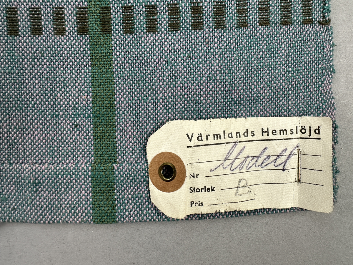 Rutigt förkläde, handvävt i tuskaft och med munkabältesvariation av bomullsgarn. Förklädet har tre inåt lagda veck 1,8cm djupa med 3cm mellanrum på var sida om mitten. Linningen, gjord av dubbla handvävda band i varprips av bomullsgarn, är fastsydda med smygstygn längs tre sidor och upptill med kaststygn. Framsidans band fortsätter som knytband 62 och 63cm på var sida. Nertill har förklädet en dubbelvikt fåll 2,2cm bred sydd med smygstygn och kortsidorna med kaststygn. På högra sidan finns en utanpå ficka, som är fastsydd med 2 parallella raksömmar. Upptill har fickan en dubbelvikt fåll 1,3cm bred sydd med smygstygn.