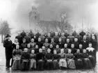 Konfirmander med präst, uppställda en bit ifrån kyrkan för fotografering. Ca. 1905, okänd plats, troligen Kronobergs län.