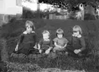 Tre sittande barn på filt på gräsmattan i en trädgård, ca. 1920.