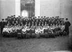 Konfirmander och präst samlade för foto utanför kyrka, ca. 1914. Okänd plats i Kronobergs län.