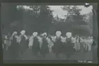 Uppvisning av folkdans på en gräsmatta/ äng. Dansarna bär folkdräkt.
