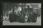 Grupporträtt av ett bröllopssällkap, fotograferade utanför ett hus vintertid.
