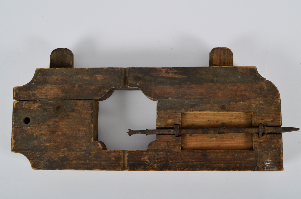 Furu. Snekret. Tilnærmet rektangulær form, innskjæringer ved tre av hjørnene. Redskapet består av to trestykker føyd sammen ved hjelp av to eiketapper som er avrundet i endene. Det ene stykket har kunnet gli på tappene og har antagelig fungert som klemme. Midt på redskapet, stor, kvadratisk åpning med konvekse buer i hjørnene. Over dette, rektangulær nedsenkning, på langs av denne er festet jernbor ved hjelp av to jernbøyler, festet på baksiden med skruegjenger og muttere. Tverrgående hulkil på hver side av den kvadratiske åpningen.