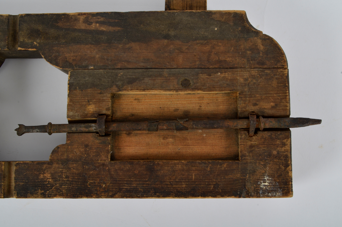 Furu. Snekret. Tilnærmet rektangulær form, innskjæringer ved tre av hjørnene. Redskapet består av to trestykker føyd sammen ved hjelp av to eiketapper som er avrundet i endene. Det ene stykket har kunnet gli på tappene og har antagelig fungert som klemme. Midt på redskapet, stor, kvadratisk åpning med konvekse buer i hjørnene. Over dette, rektangulær nedsenkning, på langs av denne er festet jernbor ved hjelp av to jernbøyler, festet på baksiden med skruegjenger og muttere. Tverrgående hulkil på hver side av den kvadratiske åpningen.