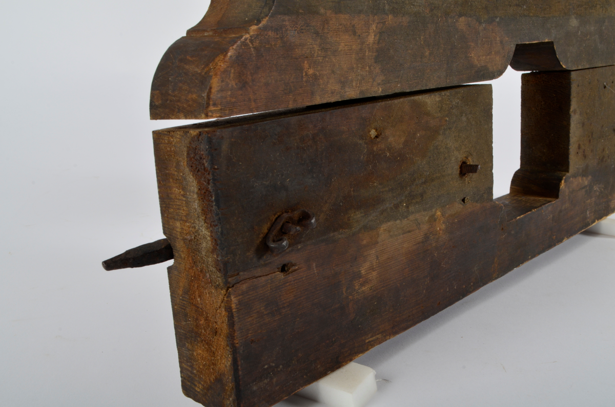 Furu. Snekret. Tilnærmet rektangulær form, innskjæringer ved tre av hjørnene. Redskapet består av to trestykker føyd sammen ved hjelp av to eiketapper som er avrundet i endene. Det ene stykket har kunnet gli på tappene og har antagelig fungert som klemme. Midt på redskapet, stor, kvadratisk åpning med konvekse buer i hjørnene. Over dette, rektangulær nedsenkning, på langs av denne er festet jernbor ved hjelp av to jernbøyler, festet på baksiden med skruegjenger og muttere. Tverrgående hulkil på hver side av den kvadratiske åpningen.