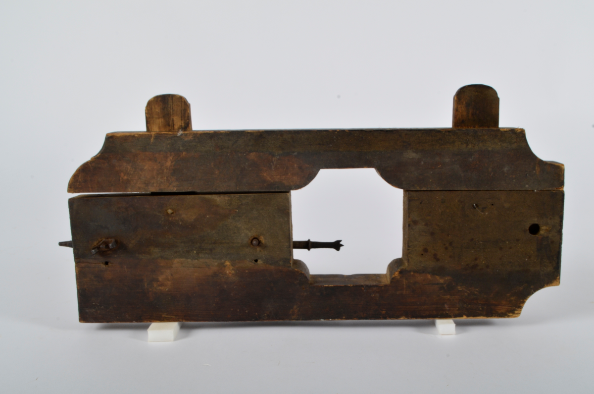 Furu. Snekret. Tilnærmet rektangulær form, innskjæringer ved tre av hjørnene. Redskapet består av to trestykker føyd sammen ved hjelp av to eiketapper som er avrundet i endene. Det ene stykket har kunnet gli på tappene og har antagelig fungert som klemme. Midt på redskapet, stor, kvadratisk åpning med konvekse buer i hjørnene. Over dette, rektangulær nedsenkning, på langs av denne er festet jernbor ved hjelp av to jernbøyler, festet på baksiden med skruegjenger og muttere. Tverrgående hulkil på hver side av den kvadratiske åpningen.