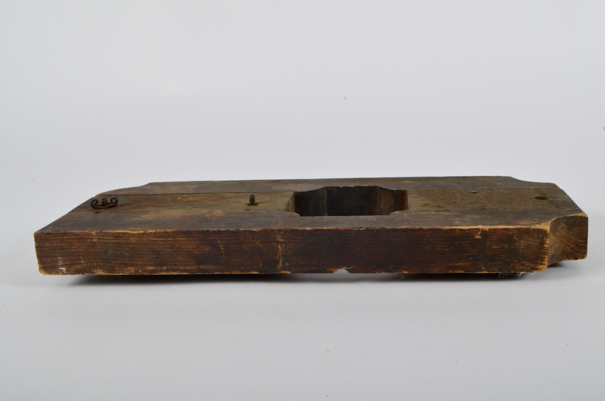 Furu. Snekret. Tilnærmet rektangulær form, innskjæringer ved tre av hjørnene. Redskapet består av to trestykker føyd sammen ved hjelp av to eiketapper som er avrundet i endene. Det ene stykket har kunnet gli på tappene og har antagelig fungert som klemme. Midt på redskapet, stor, kvadratisk åpning med konvekse buer i hjørnene. Over dette, rektangulær nedsenkning, på langs av denne er festet jernbor ved hjelp av to jernbøyler, festet på baksiden med skruegjenger og muttere. Tverrgående hulkil på hver side av den kvadratiske åpningen.