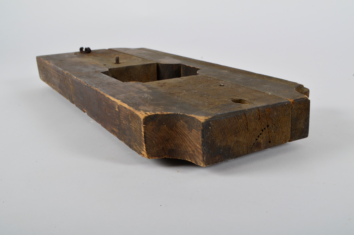 Furu. Snekret. Tilnærmet rektangulær form, innskjæringer ved tre av hjørnene. Redskapet består av to trestykker føyd sammen ved hjelp av to eiketapper som er avrundet i endene. Det ene stykket har kunnet gli på tappene og har antagelig fungert som klemme. Midt på redskapet, stor, kvadratisk åpning med konvekse buer i hjørnene. Over dette, rektangulær nedsenkning, på langs av denne er festet jernbor ved hjelp av to jernbøyler, festet på baksiden med skruegjenger og muttere. Tverrgående hulkil på hver side av den kvadratiske åpningen.