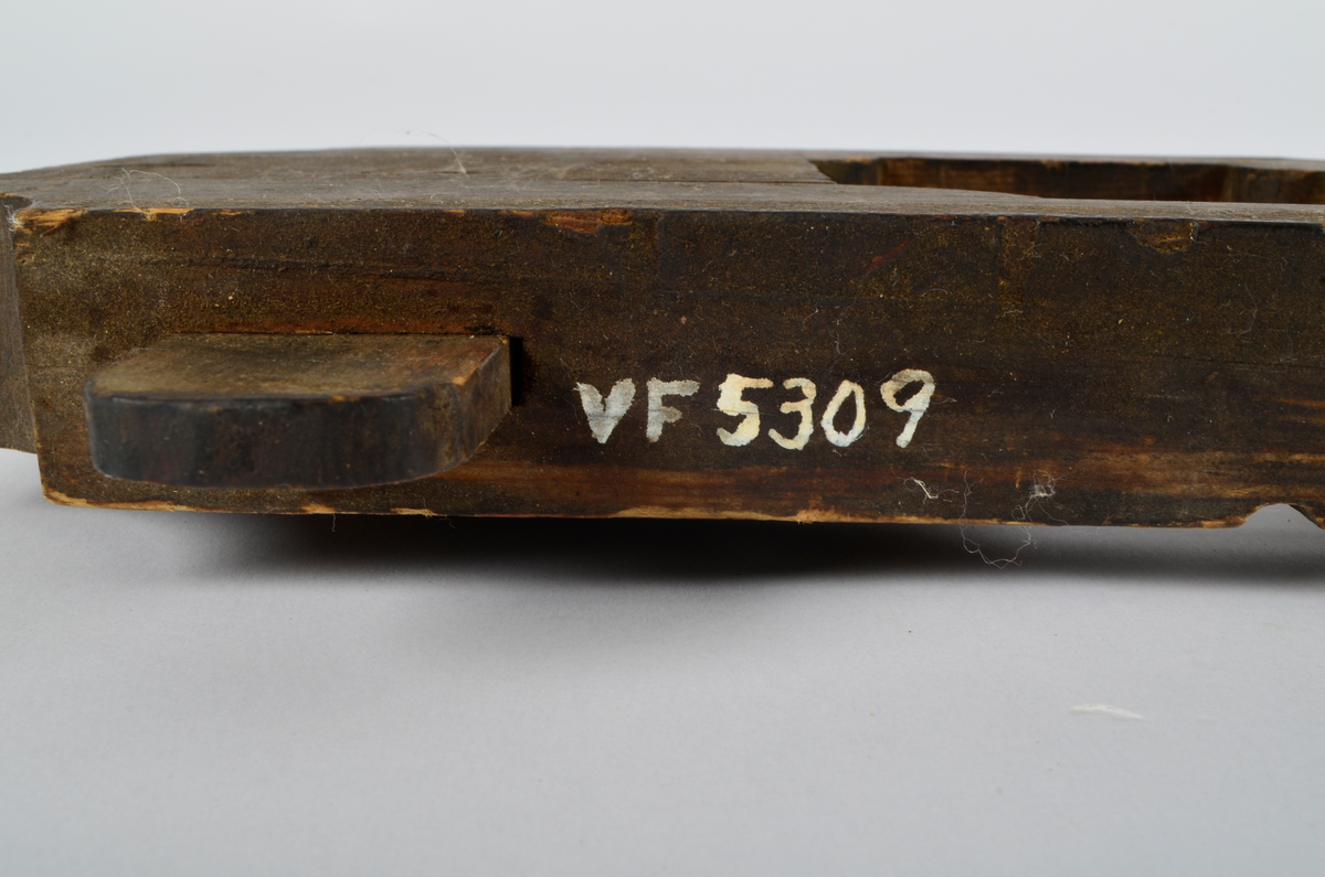 Furu. Snekret. Tilnærmet rektangulær form, innskjæringer ved tre av hjørnene. Redskapet består av to trestykker føyd sammen ved hjelp av to eiketapper som er avrundet i endene. Det ene stykket har kunnet gli på tappene og har antagelig fungert som klemme. Midt på redskapet, stor, kvadratisk åpning med konvekse buer i hjørnene. Over dette, rektangulær nedsenkning, på langs av denne er festet jernbor ved hjelp av to jernbøyler, festet på baksiden med skruegjenger og muttere. Tverrgående hulkil på hver side av den kvadratiske åpningen.