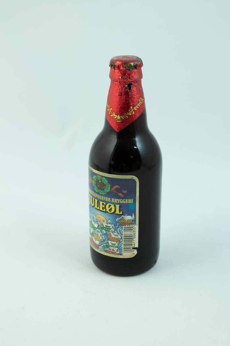 Brun glassflaske med flerfarget etikett med julemotiv. En snødekt landsby.