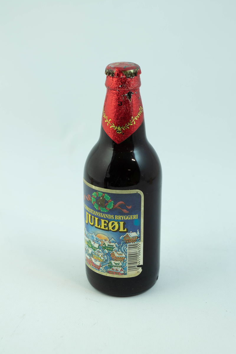 Brun glassflaske med flerfarget etikett med julemotiv. En snødekt landsby.