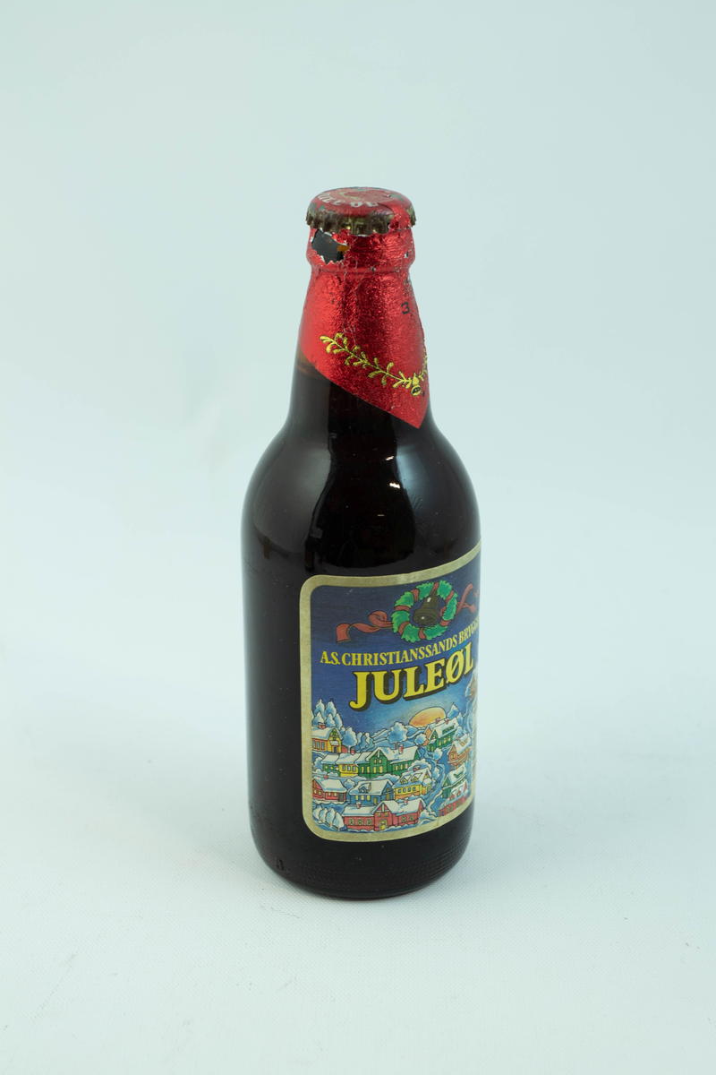 Brun glassflaske med flerfarget etikett med julemotiv. En snødekt landsby.