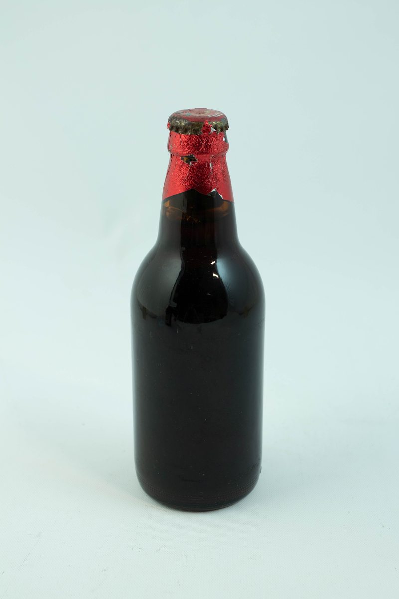 Brun glassflaske med flerfarget etikett med julemotiv. En snødekt landsby.