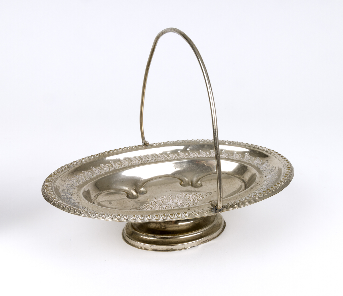 Skål. Oval og flat skål i form av en kurv, med håndtak og fot. Tynn metalltrådhåndtak fast på langsidene. Gravert dekor med plantemotiver med blomster og blader. Akantusblader som dekor midt i fatet.
