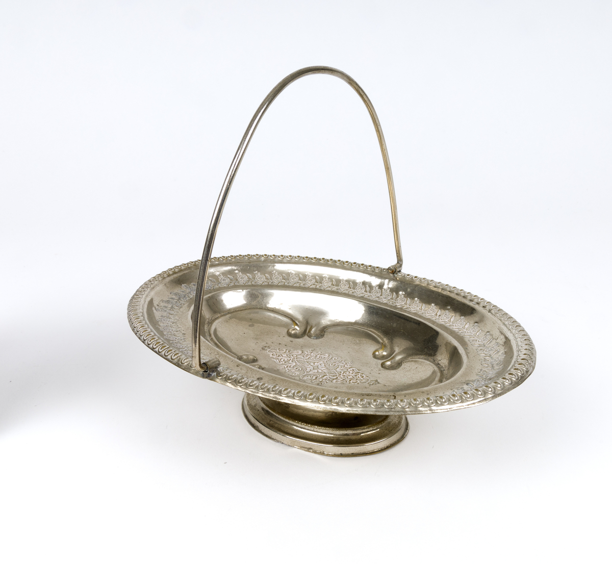 Skål. Oval og flat skål i form av en kurv, med håndtak og fot. Tynn metalltrådhåndtak fast på langsidene. Gravert dekor med plantemotiver med blomster og blader. Akantusblader som dekor midt i fatet.