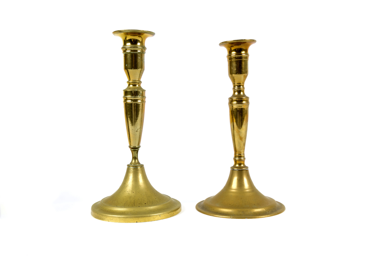 To enarmede lysestake i messing med rund fot, smalt balusterformet skaf og kort sylindrisk lyspipe med krage. Rund fotplate prydet med 2 opphøyde, konsentriske sirkler. Forhøyet midte. Begge to er like, men forskjellige i detaljene i deres dreieform.