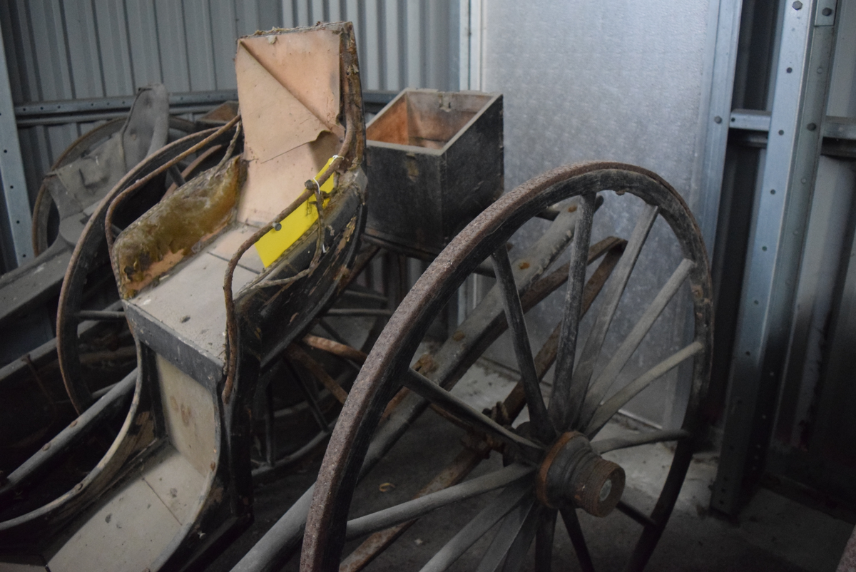 Kjerre med to hjul på aksling. Hjul av tre med 14 eiker og jernskoning. Aksling med bue, firkantet i endene. Polstret sete (polstring delvis borte) med rygg og armlener. Trebrett for skjerming mot stein og støv foran sete. Stigbøyler av jern. Liten oppbevaringskasse bak setet.