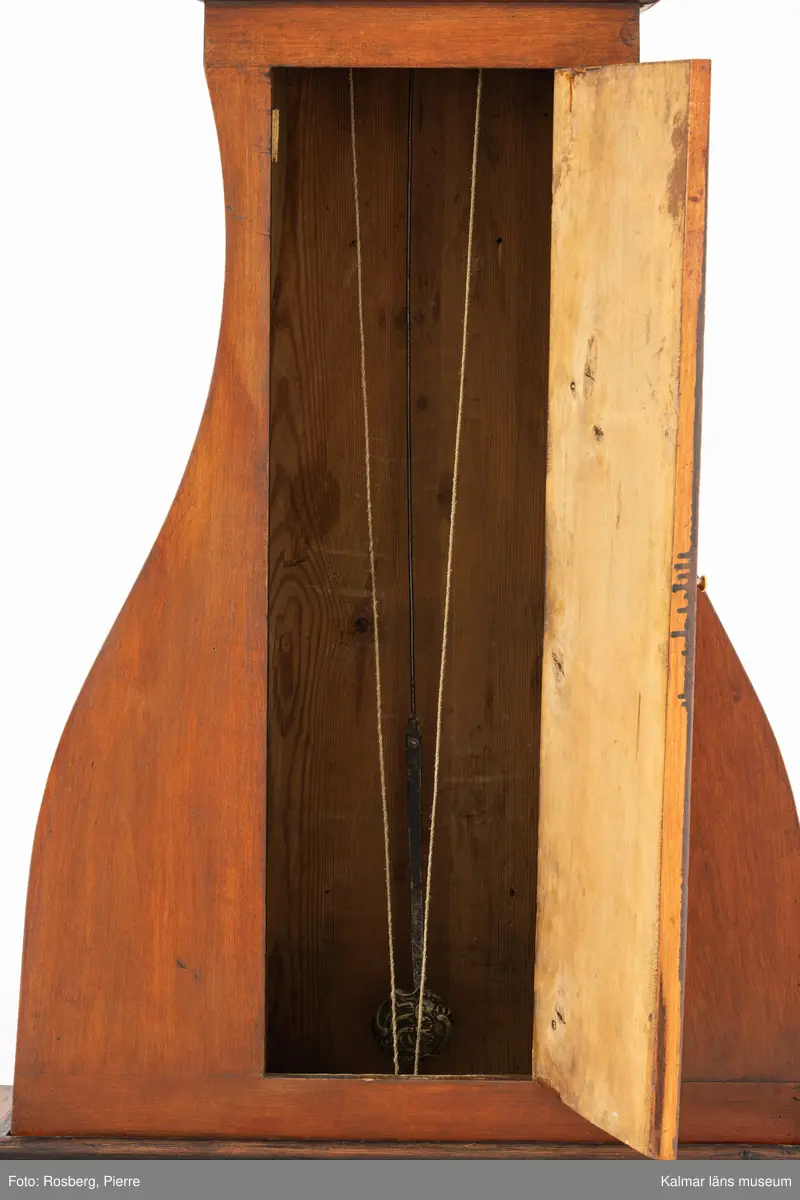 KLM 11514. Golvur. Snedklaffbyrå med klockfodral och urverk. Av furu betsat i brunt med svartmålade detaljer. Nedre delen av golvuret i form av en snedklaffbyrå med fyra lådor samt snedklaff, inuti med smålådor. Klockfodralet är fiolformat med dörr mitt på. Rund öppning för urtavlan, huvens glas saknas. Urtavla och visare av metall. Urtavlan målad i vitt med svarta siffror och signerad i svart: A.A.S. Mora. Urverk av stål och trä, tillhörande nyckel finns. Pendel med rund platta av mässing i form av en rocaille. Lod saknas.