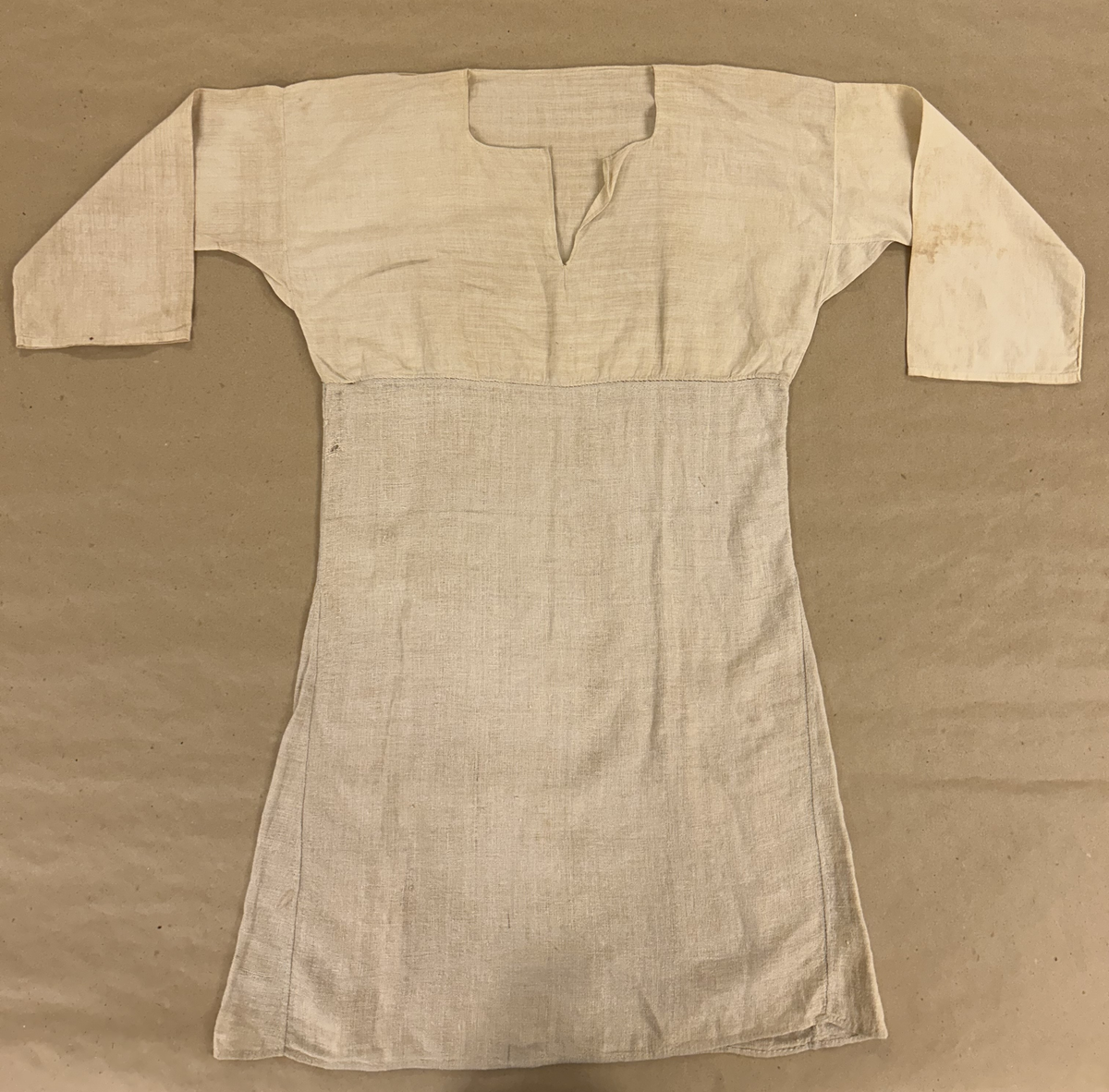 Särk i vitt, tuskaftat linne. Livet skuret i ett rakt stycke, ingen axelsöm. Sprund framtill, rundad halsringning. Rakt skuren ärm med spjäll. Nedre delen av grövre lingarn påsydd på livet strax neranför sprundet. Isydda kilar i sidsömmarna.