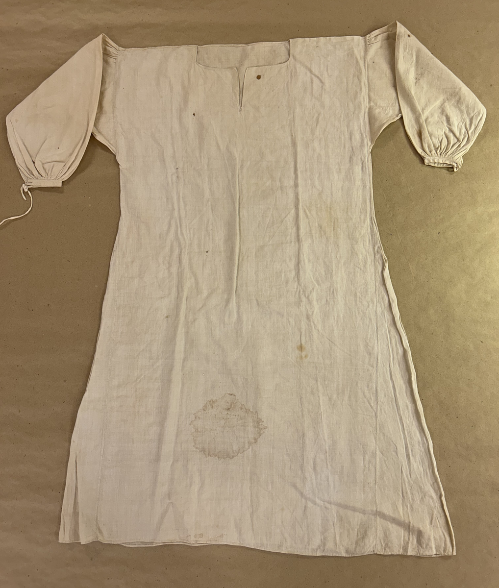 Särk av tuskaftat linne. Fram- och bakstycke av ett sammanhängande stycke isydda kilar i sidosömmen. Förstärkning över axlarna, sprund framtil. Rundad halsringning. Rak ärm med spjäll, rynkad mot axeln och handlinning. Tränsade knapphål och sydda prickstickstygn på linningen, knytband.