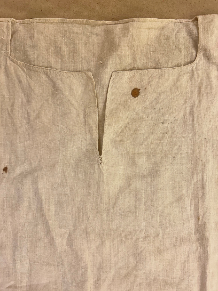 Särk av tuskaftat linne. Fram- och bakstycke av ett sammanhängande stycke isydda kilar i sidosömmen. Förstärkning över axlarna, sprund framtil. Rundad halsringning. Rak ärm med spjäll, rynkad mot axeln och handlinning. Tränsade knapphål och sydda prickstickstygn på linningen, knytband.