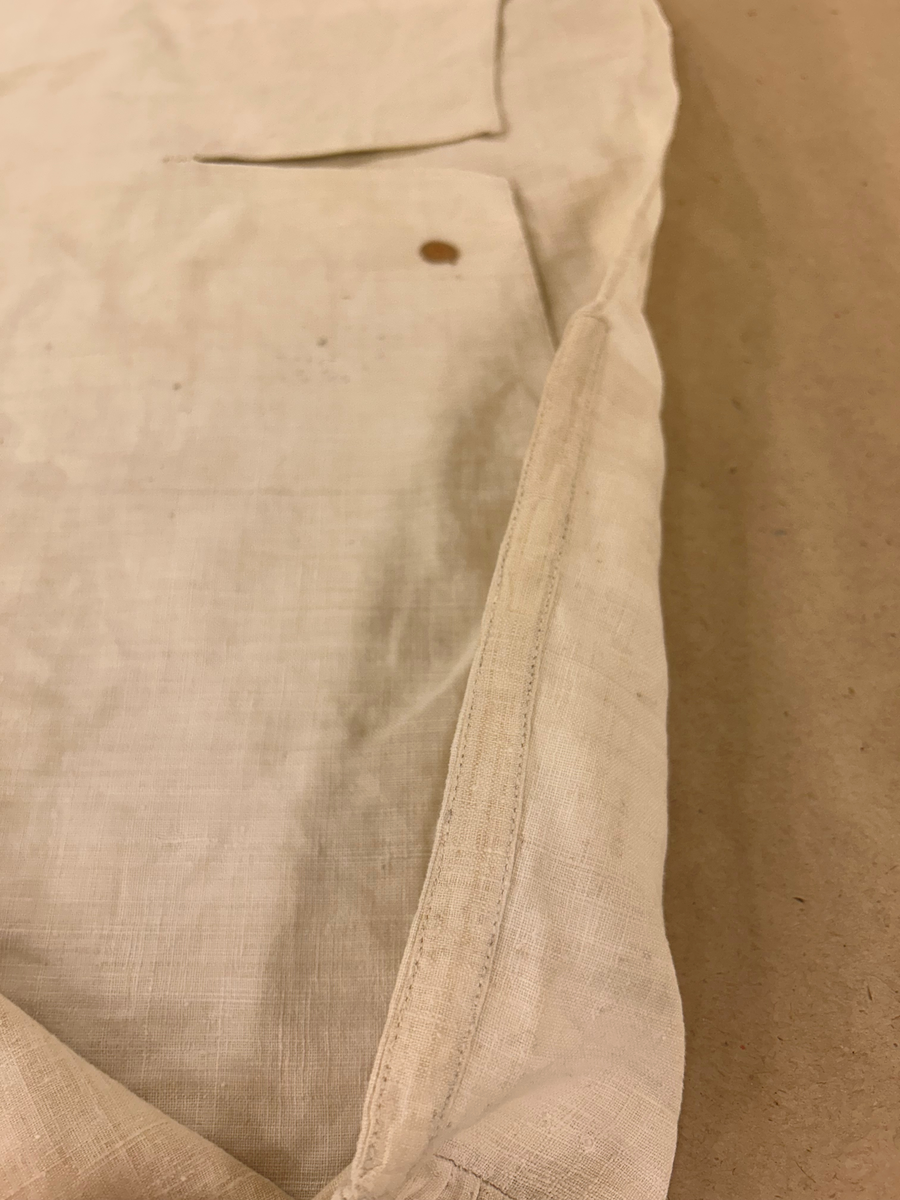 Särk av tuskaftat linne. Fram- och bakstycke av ett sammanhängande stycke isydda kilar i sidosömmen. Förstärkning över axlarna, sprund framtil. Rundad halsringning. Rak ärm med spjäll, rynkad mot axeln och handlinning. Tränsade knapphål och sydda prickstickstygn på linningen, knytband.