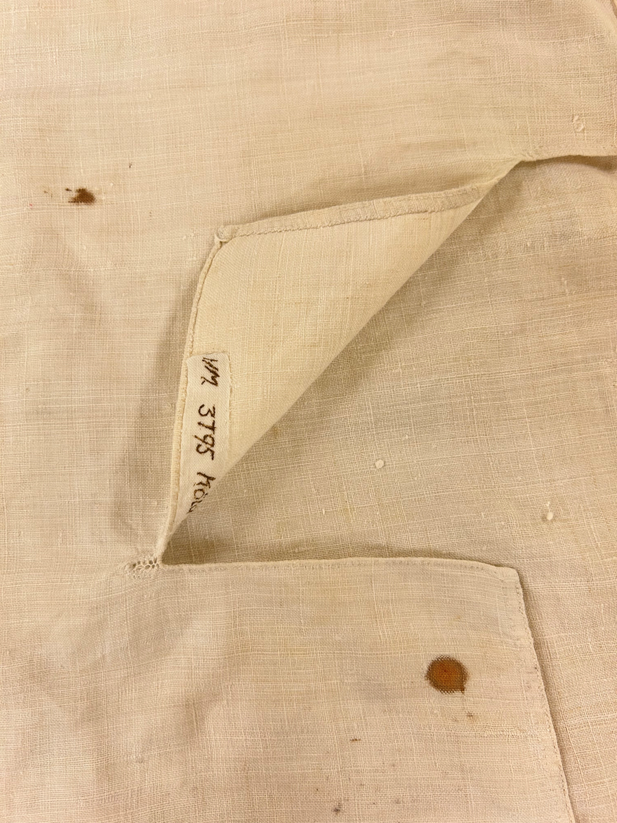 Särk av tuskaftat linne. Fram- och bakstycke av ett sammanhängande stycke isydda kilar i sidosömmen. Förstärkning över axlarna, sprund framtil. Rundad halsringning. Rak ärm med spjäll, rynkad mot axeln och handlinning. Tränsade knapphål och sydda prickstickstygn på linningen, knytband.