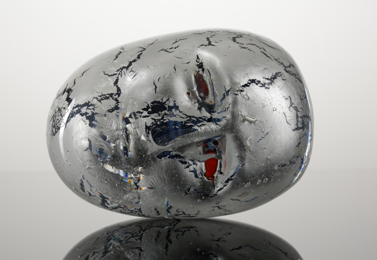 Prydnadsföremål i form av ett ansikte.
Silverfolierat med röda ögon.