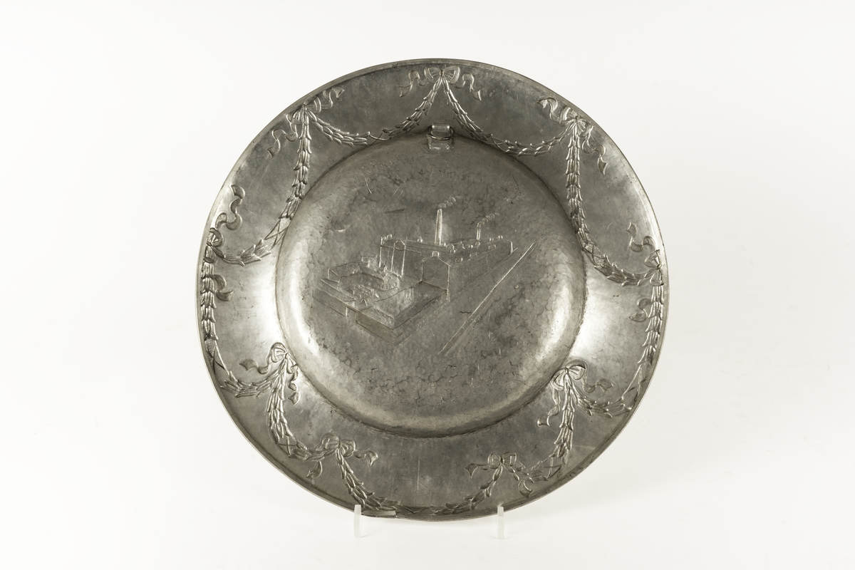 Ett dekorerat tennfat som överlämnades som födelsedagsgåva till Alfred Ehnström (?) år 1926 i samband med hans 70-årsfirande. Centralmotivet på fatet avbildar Pixfabriken. På brämet finns formgivarens namnstämpel: Astri Ekengren.