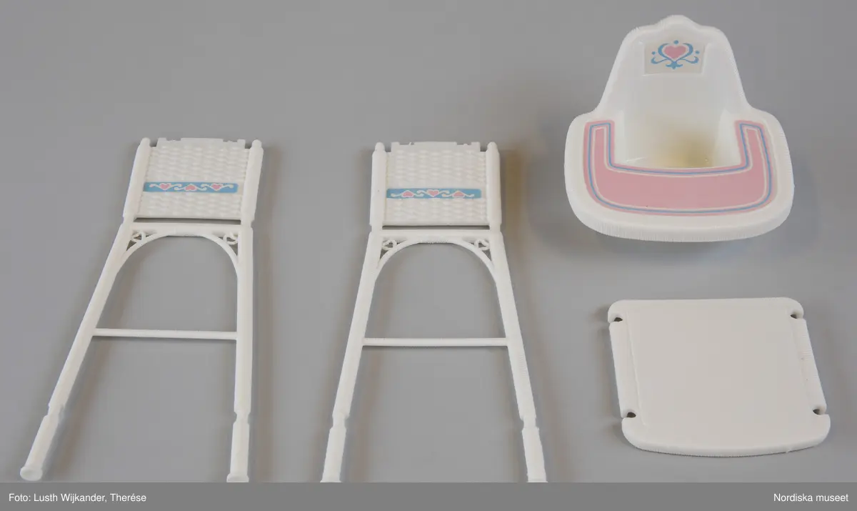 Inventering Sesam 1996-1999:H 2,5-20,5 cm
Barnkammarmöbel och tillbehör till "the Heart Family", allt av plast och syntettextil.
Består av: Säng/badkar i tre delar av, vit. bäddutrustning (=madrass, madrassöverdrag, täcke, kudde, sängomhänge). Vit barnstol. 2 st haklappar. Nallebjörn i bil, rosa och gul i tre delar (vid inv. 1998 saknas 2 del). Boll. Papperskorg ((saknas vid inv. 1998) med lock. Gul sked. Gul skallra. Docka (saknas vid inv. 1998). Bricka. Tallrik. 2 st muggar. 2 st nappflaskor. Tvål. Badanka. Tvättlappa av blå frott¿. Handduk av rosa frott¿.
Originalkartong av kartong med öppning i sidan, foton av föremålen tillsammans med dockor på alla sidor, text på franska, engelska, tyska och italienska. , bl a "la Famille Doucoeur / Nursery" Prislapp i ett hörn "POPPIS LEK / 349.00".  Inuti kartongen insats av brun kartong. 
Vissa av föremålen är omonterade och sitter fortfarande (alla vid inv. 1987) kvar på plastpinnar. 
Se inv.nr 313.130-313.133.
AT 1987 [=Annika Tyrfelt]
Leif Wallin 1998