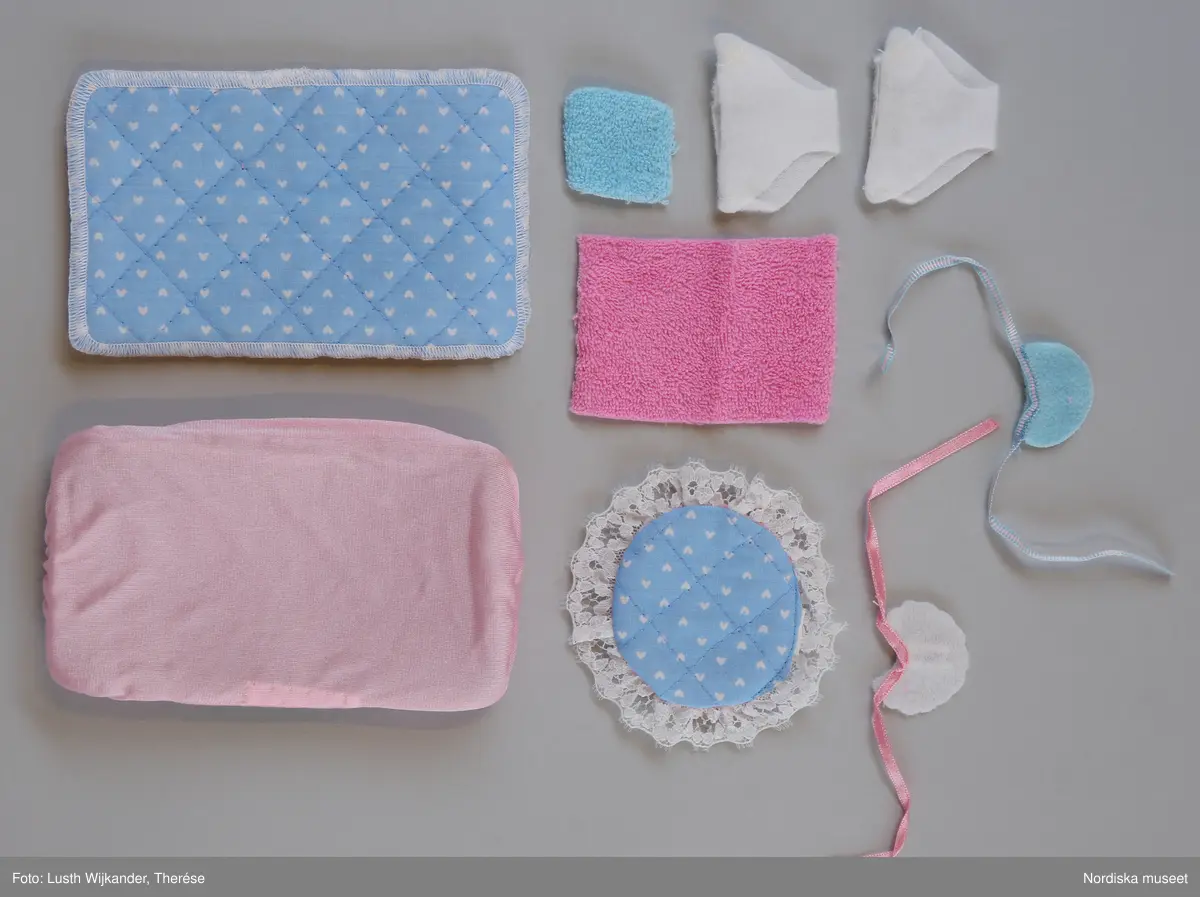 Inventering Sesam 1996-1999:H 2,5-20,5 cm
Barnkammarmöbel och tillbehör till "the Heart Family", allt av plast och syntettextil.
Består av: Säng/badkar i tre delar av, vit. bäddutrustning (=madrass, madrassöverdrag, täcke, kudde, sängomhänge). Vit barnstol. 2 st haklappar. Nallebjörn i bil, rosa och gul i tre delar (vid inv. 1998 saknas 2 del). Boll. Papperskorg ((saknas vid inv. 1998) med lock. Gul sked. Gul skallra. Docka (saknas vid inv. 1998). Bricka. Tallrik. 2 st muggar. 2 st nappflaskor. Tvål. Badanka. Tvättlappa av blå frott¿. Handduk av rosa frott¿.
Originalkartong av kartong med öppning i sidan, foton av föremålen tillsammans med dockor på alla sidor, text på franska, engelska, tyska och italienska. , bl a "la Famille Doucoeur / Nursery" Prislapp i ett hörn "POPPIS LEK / 349.00".  Inuti kartongen insats av brun kartong. 
Vissa av föremålen är omonterade och sitter fortfarande (alla vid inv. 1987) kvar på plastpinnar. 
Se inv.nr 313.130-313.133.
AT 1987 [=Annika Tyrfelt]
Leif Wallin 1998