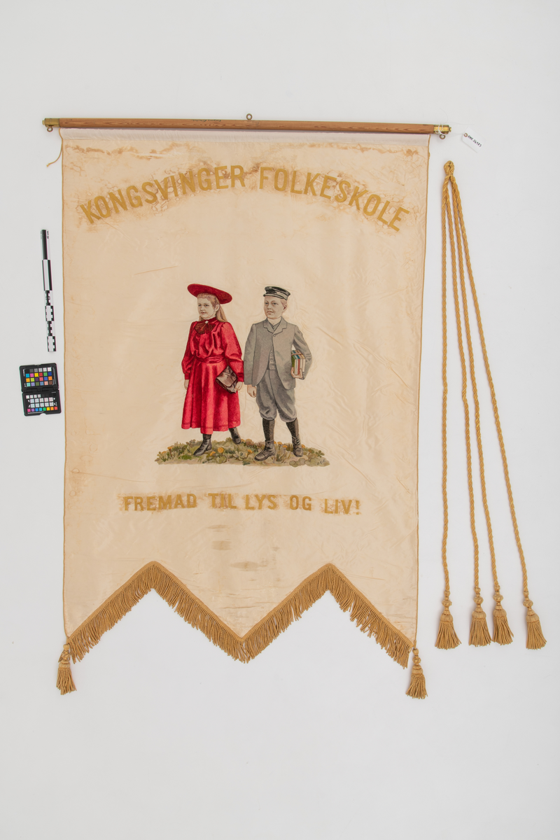 En gutt som holder skolebøker og ei jente med skoleveske er brodert midt på faneduken. Over er det brodert "Kongsvinger folkeskole" i store bokstaver. Under er det brodert "Fremad til lys og liv!" i store bokstaver.