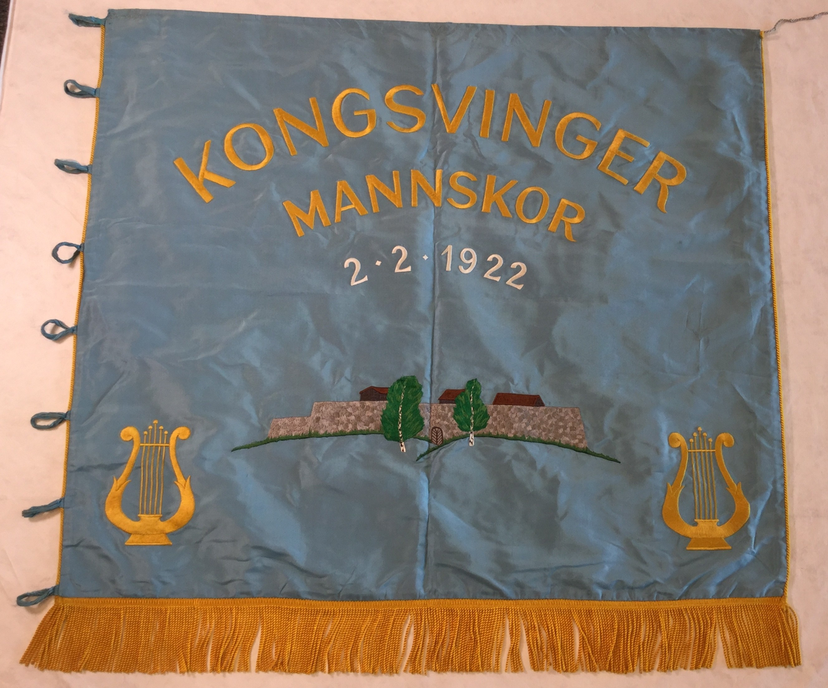 Kongsvinger festning brodert på faneduken. To lyre på hver side brodert på. Tosidig fane med samme motiv på begge sider.