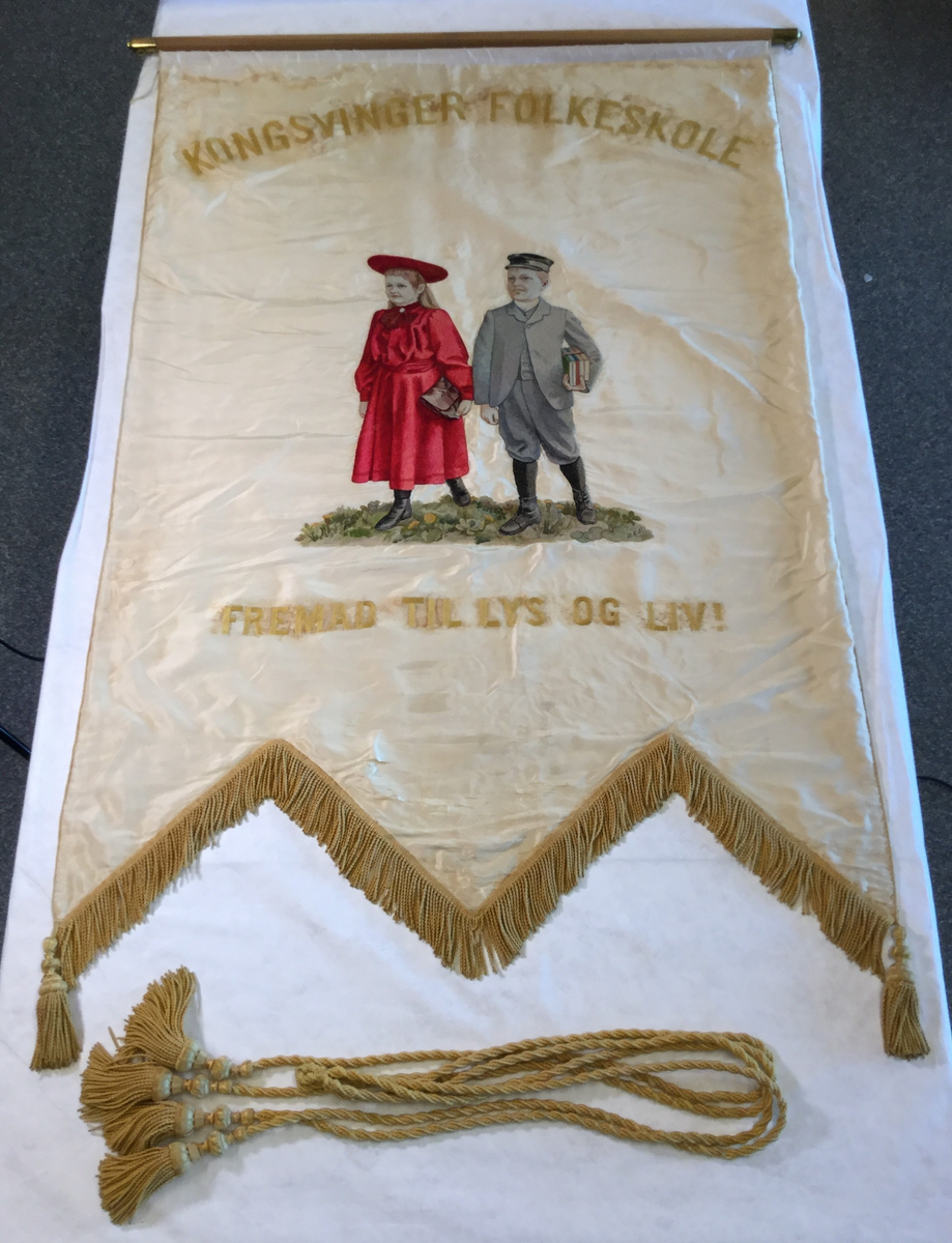 En gutt som holder skolebøker og ei jente med skoleveske er brodert midt på faneduken. Over er det brodert "Kongsvinger folkeskole" i store bokstaver. Under er det brodert "Fremad til lys og liv!" i store bokstaver.