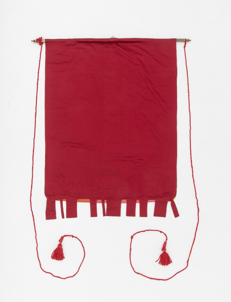 Abstrakt motiv med mennesker på vei mot betrakteren i forgrunnen. I bakgrunnen er det trær. Holt ungdomsskole 1975 i store bokstaver er sydd på høyre side på faneduken.