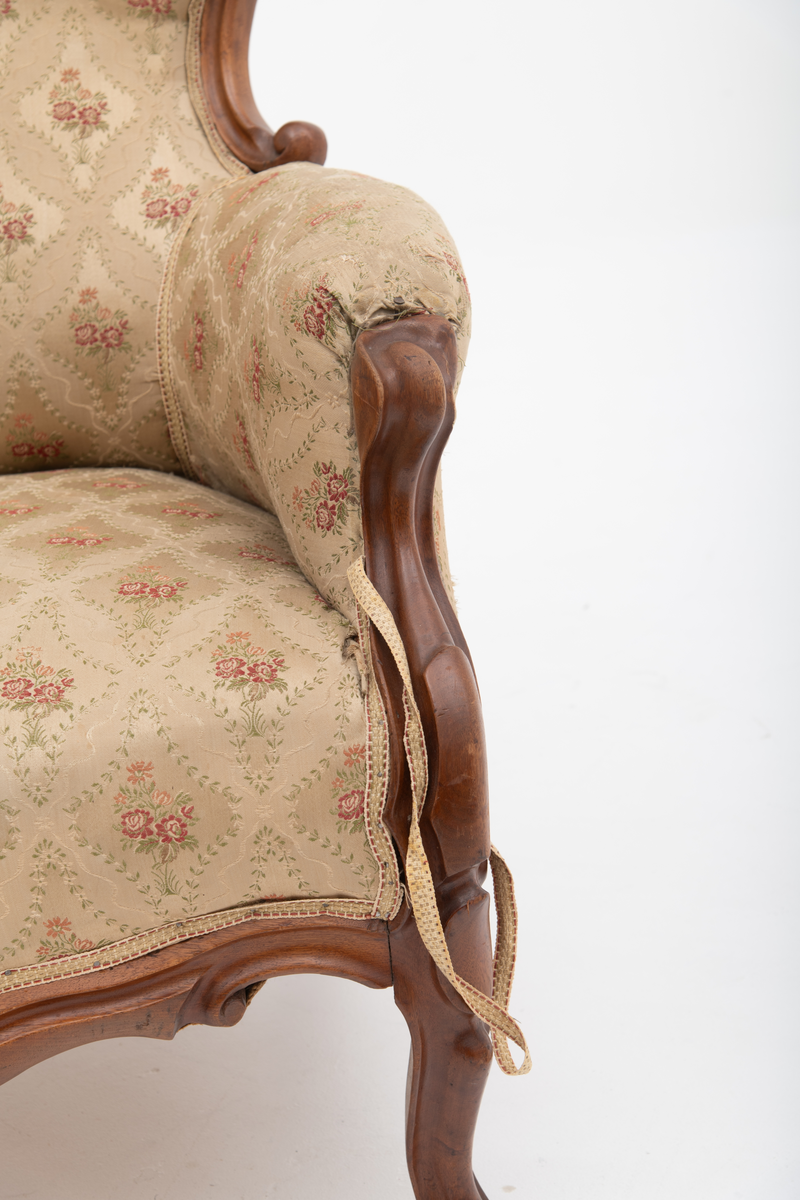 Gruppe med sofa, to lenestoler og tre mindre stoler uten armlener i stilen nyrokokko. Gyllengult trekk med rosemotiv og mørkt treverk med buede, organiske linjer.
