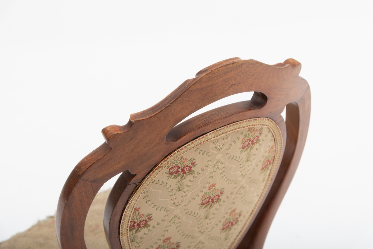 Gruppe med sofa, to lenestoler og tre mindre stoler uten armlener i stilen nyrokokko. Gyllengult trekk med rosemotiv og mørkt treverk med buede, organiske linjer.
