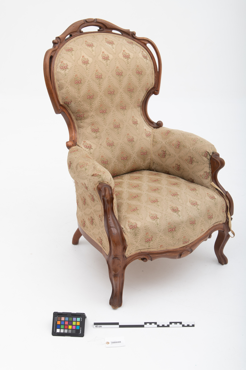 Gruppe med sofa, to lenestoler og tre mindre stoler uten armlener i stilen nyrokokko. Gyllengult trekk med rosemotiv og mørkt treverk med buede, organiske linjer.
