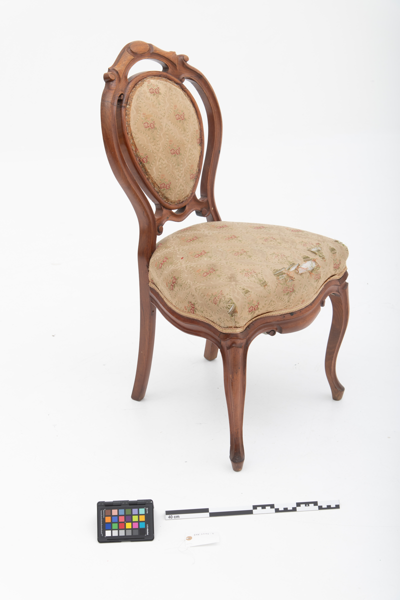 Gruppe med sofa, to lenestoler og tre mindre stoler uten armlener i stilen nyrokokko. Gyllengult trekk med rosemotiv og mørkt treverk med buede, organiske linjer.
