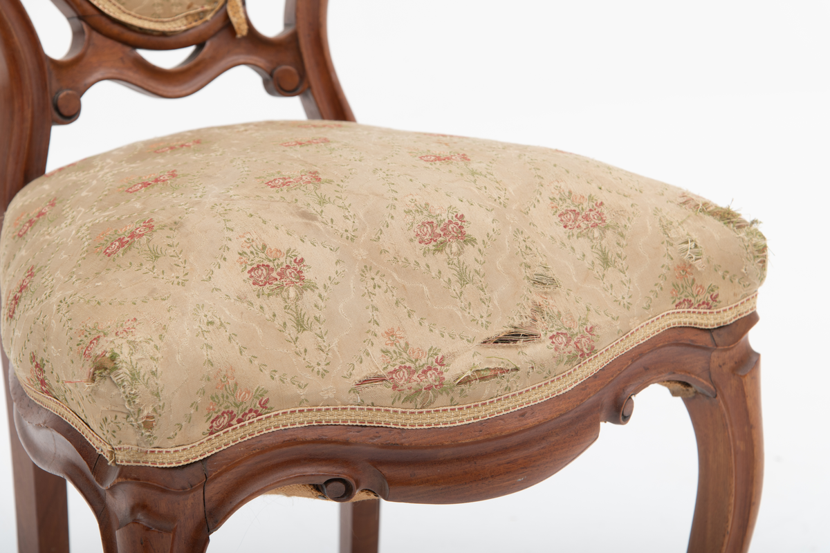 Gruppe med sofa, to lenestoler og tre mindre stoler uten armlener i stilen nyrokokko. Gyllengult trekk med rosemotiv og mørkt treverk med buede, organiske linjer.
