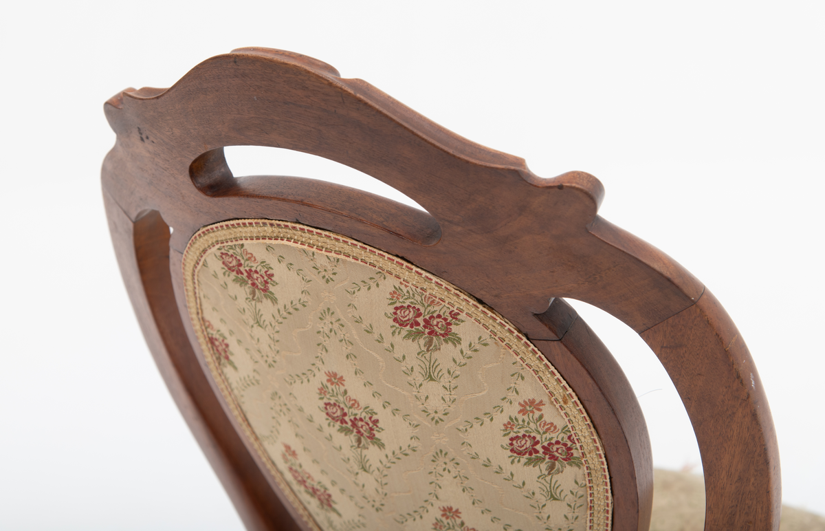 Gruppe med sofa, to lenestoler og tre mindre stoler uten armlener i stilen nyrokokko. Gyllengult trekk med rosemotiv og mørkt treverk med buede, organiske linjer.

